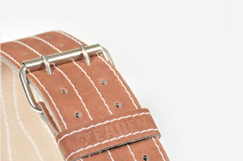 Close-up of a brown cowhide weight lifting belt featuring metal buckle and white stitching for durability.